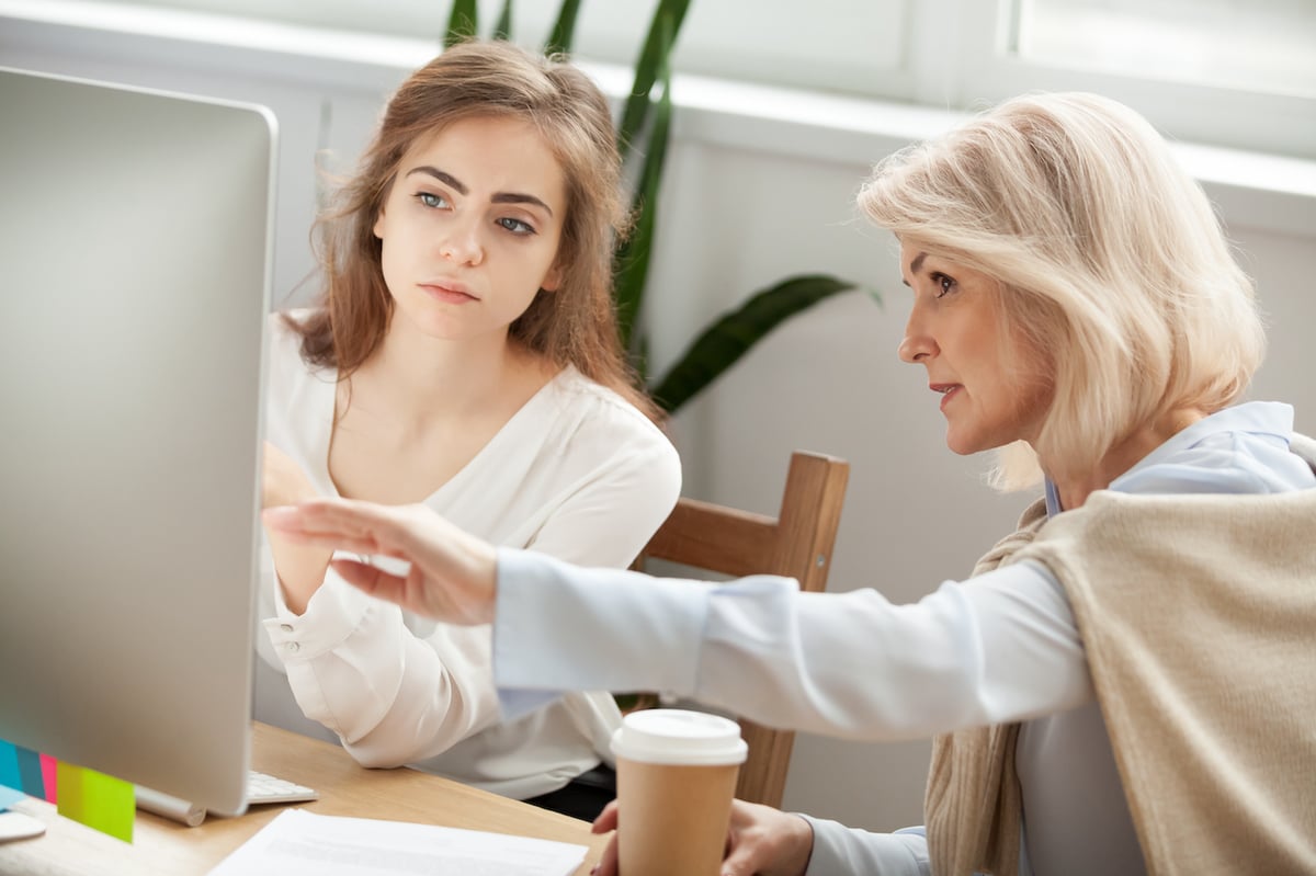 Director of a childcare enterprise mentoring a younger employee at a computer